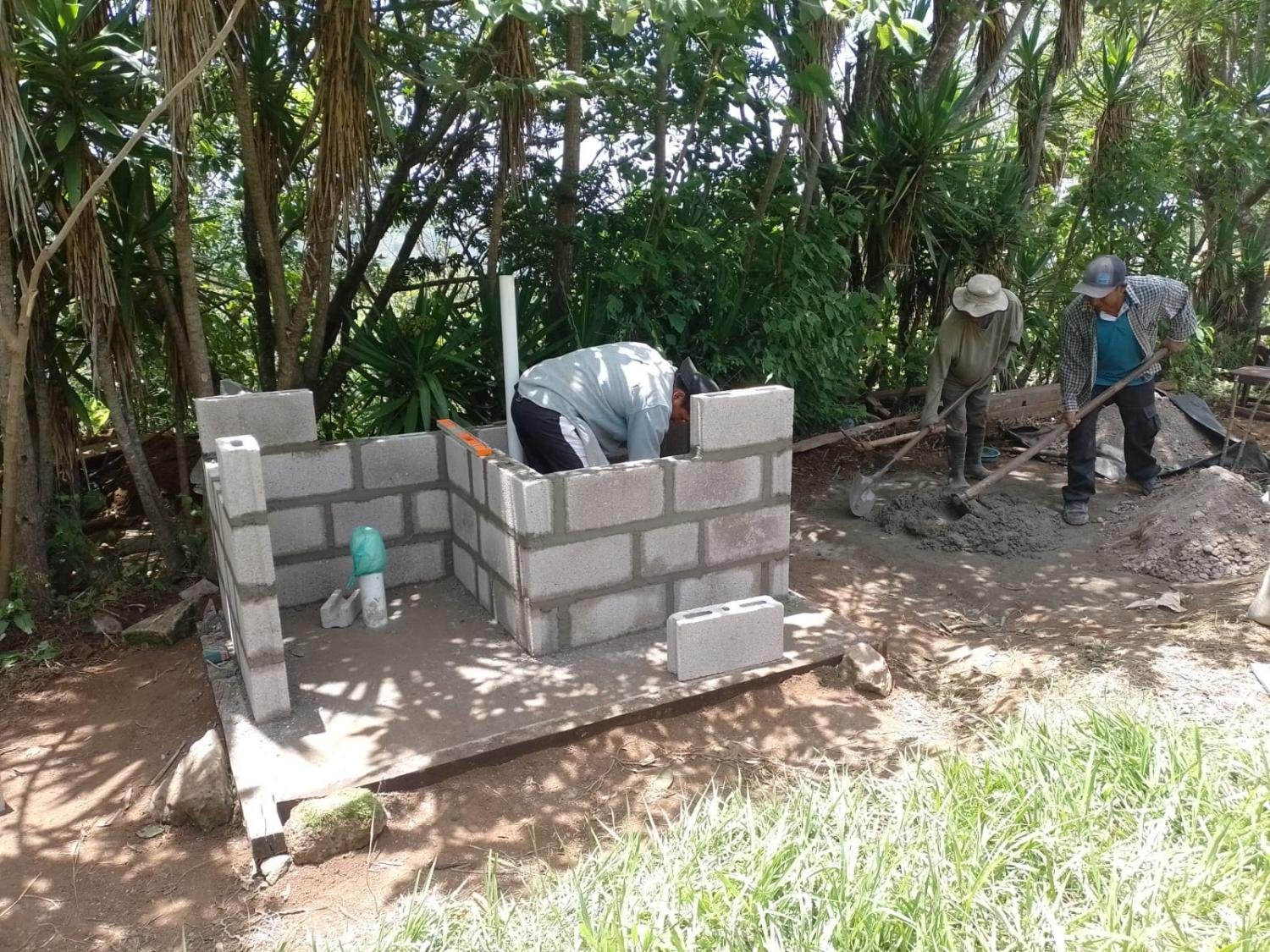 Neighbors in Honduras laying concrete block to build a safe latrine in the shade of trees.