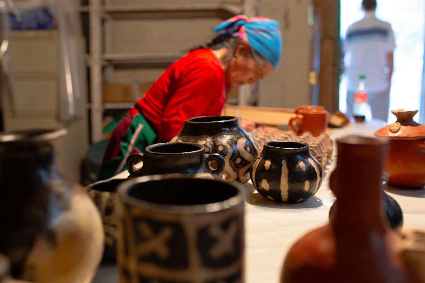 A Lenca artisan at her pottery table, with traditional vessels in the foreground.