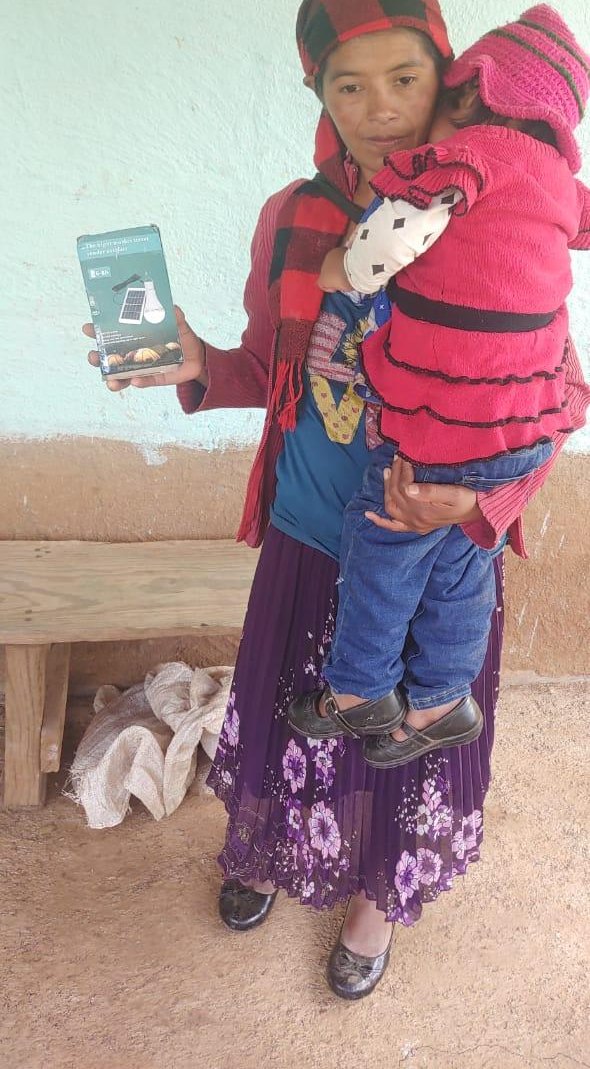 A Lenca mother holding her child and a solar lamp, standing in front of her home.